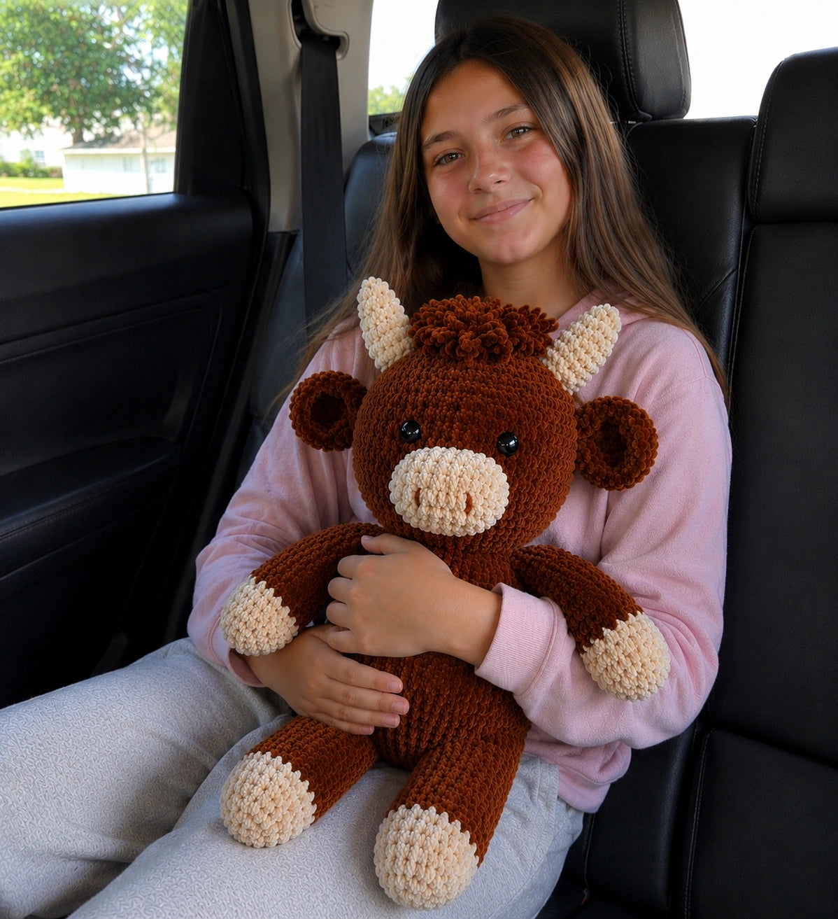 Large handmade crochet Highland cow plush held by a 12-year-old girl inside a car