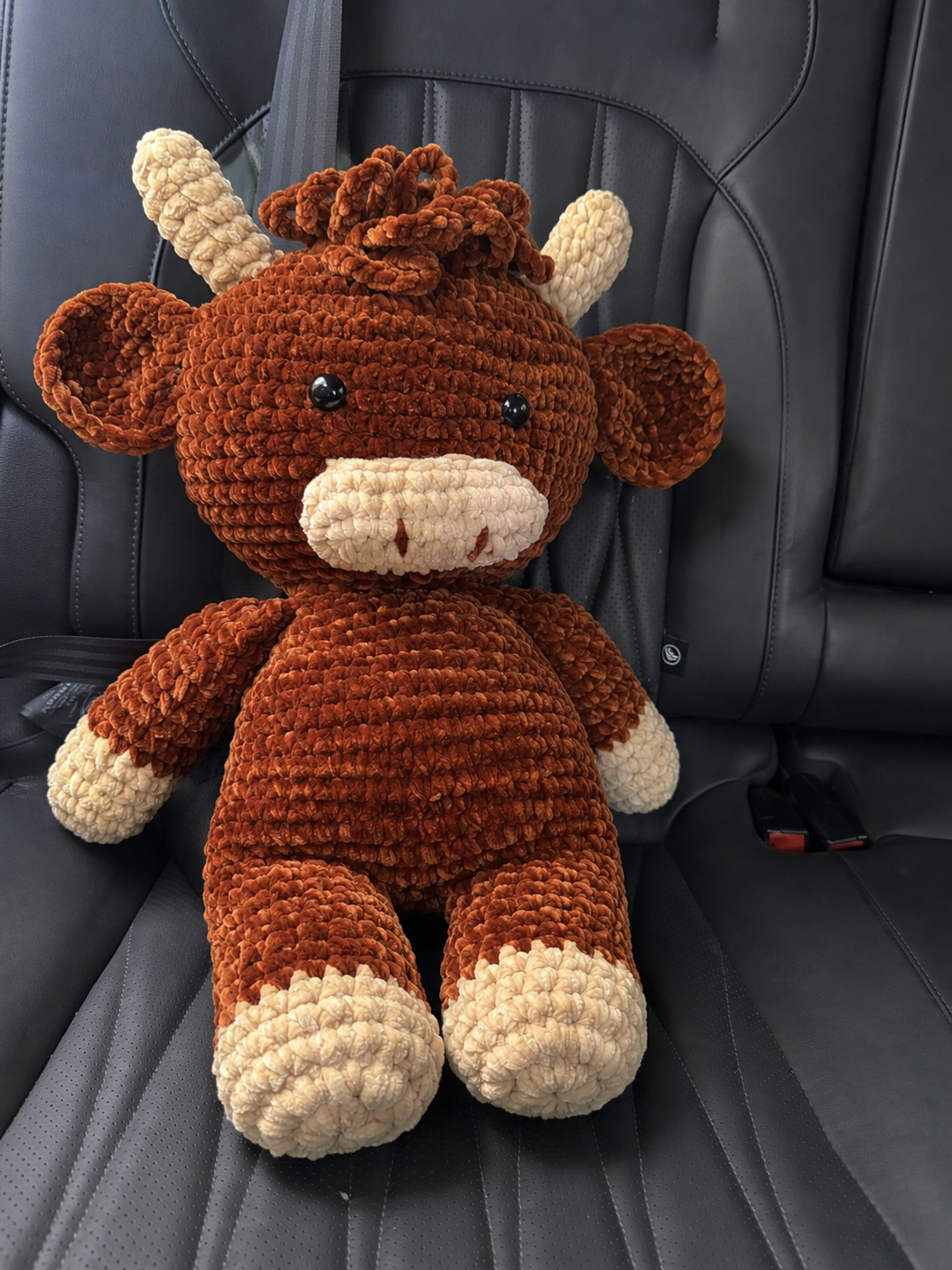 Handmade crochet Highland cow plush sitting in a car as a cozy travel companion